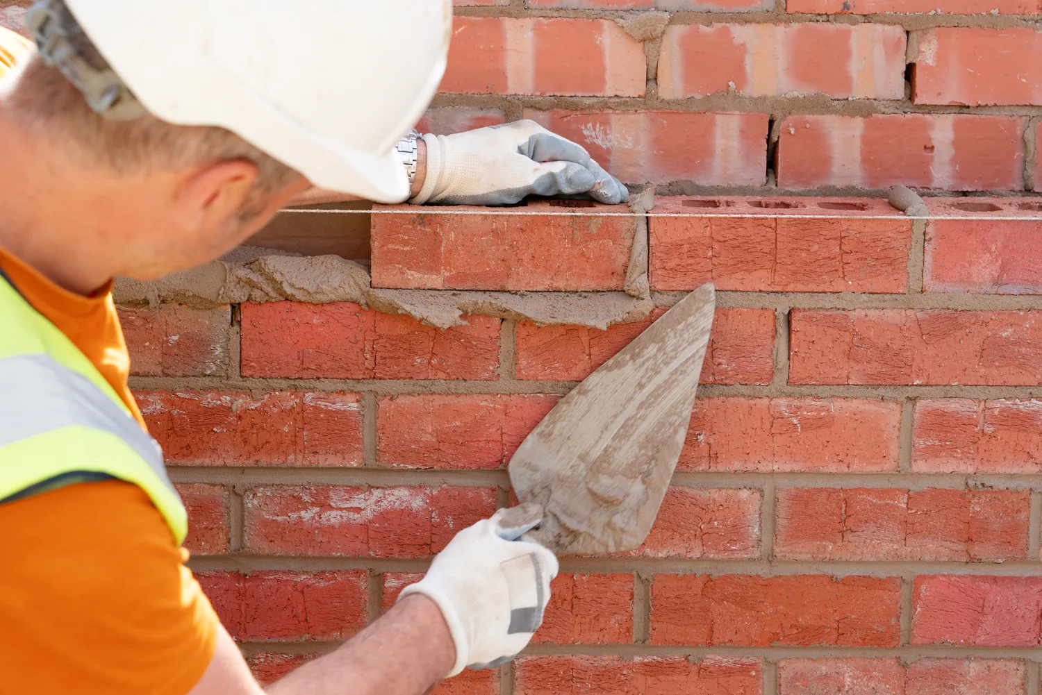 Bauunternehmen Schäfer - Maurer verlegen Ziegel auf Mörtel bei einem neuen Wohnhausbau. Erwerben Sie den NVQ-Abschluss im Maurerhandwerk